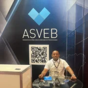 Uátila Martins, presidente da ASVEB (Associação das Serralherias e Vidraçarias do Estado da Bahia), sentado em um estande durante a feira FESQUA 2026. Ao fundo, painel com a logomarca da ASVEB, slogan oficial e um QR Code promocional da associação baiana.